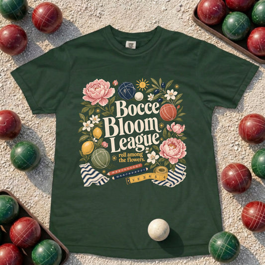 A dark green crewneck t-shirt featuring a colorful graphic design for 'Bocce Bloom League 2024', styled in a flat-lay on a sandy surface surrounded by red and green wooden bocce balls.